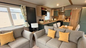 A compact living area with two grey sofas, a small table, a TV, and a kitchenette. - Vintage 121 - Southview Holiday Park Skegness (Skegness)