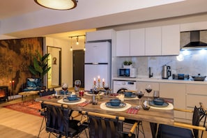 A modern kitchen with white cabinets, a dining area with a wooden table set for a meal, and a living area with a sofa and a plant. - Bosphorus View Apt With 2 Terraces At Monnas Suite (Istanbul)