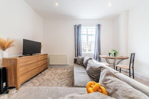 A modern living room with a sofa, a wooden cabinet, a television, a dining table with chairs, and a window with curtains. - Central - Stay 4 - Paid Parking - Near Transport (Maidstone)