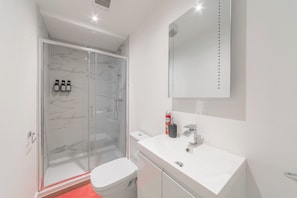 A modern bathroom with a glass-enclosed shower, a white toilet, and a sink with a mirror above.