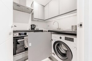 A compact kitchen with a built-in oven, a washing machine, and a coffee maker. - Central - Stay 2 - Paid Parking - Near Transport (Maidstone)