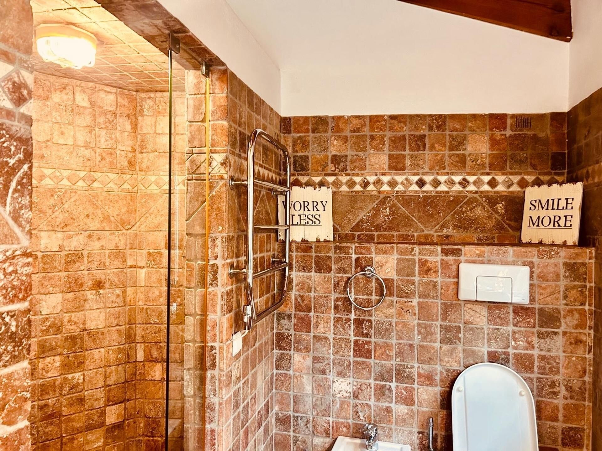 A bathroom with a tiled wall, a towel rack, a toilet, and two signs reading 'SORRY LESS' and 'SMILE MORE'.
