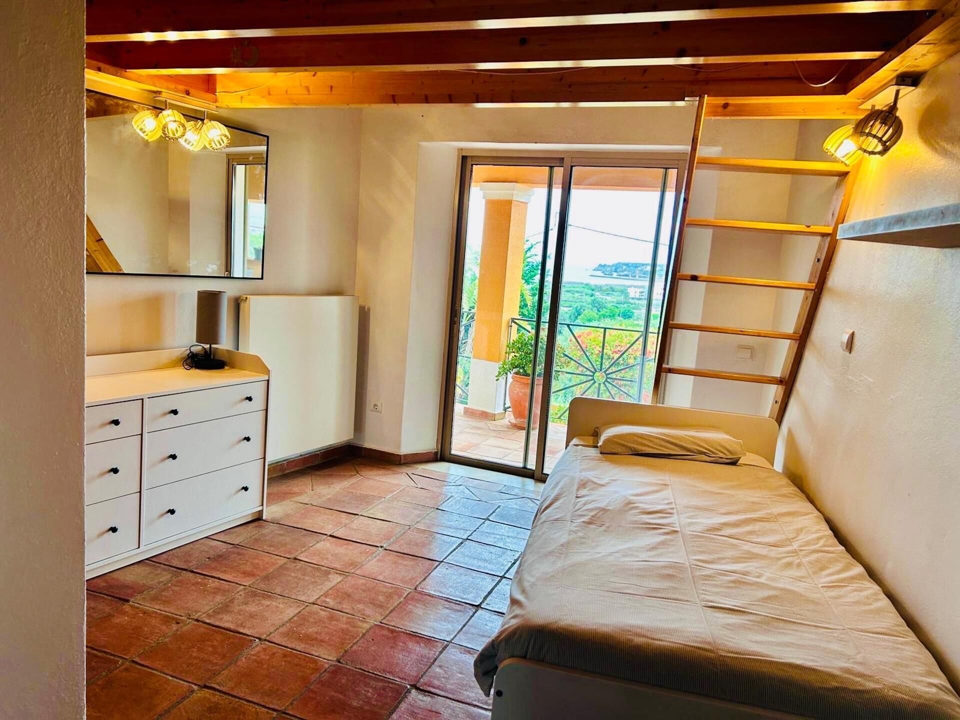 A bedroom with a bed, a dresser, a mirror, and a balcony with a view.