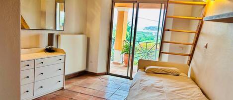 A bedroom with a bed, a dresser, a mirror, and a balcony with a view.