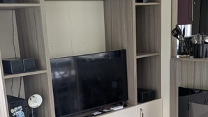 Una sala de estar moderna con televisor de pantalla plana, estantes empotrados, una cafetera y un comedor con mesa de madera.