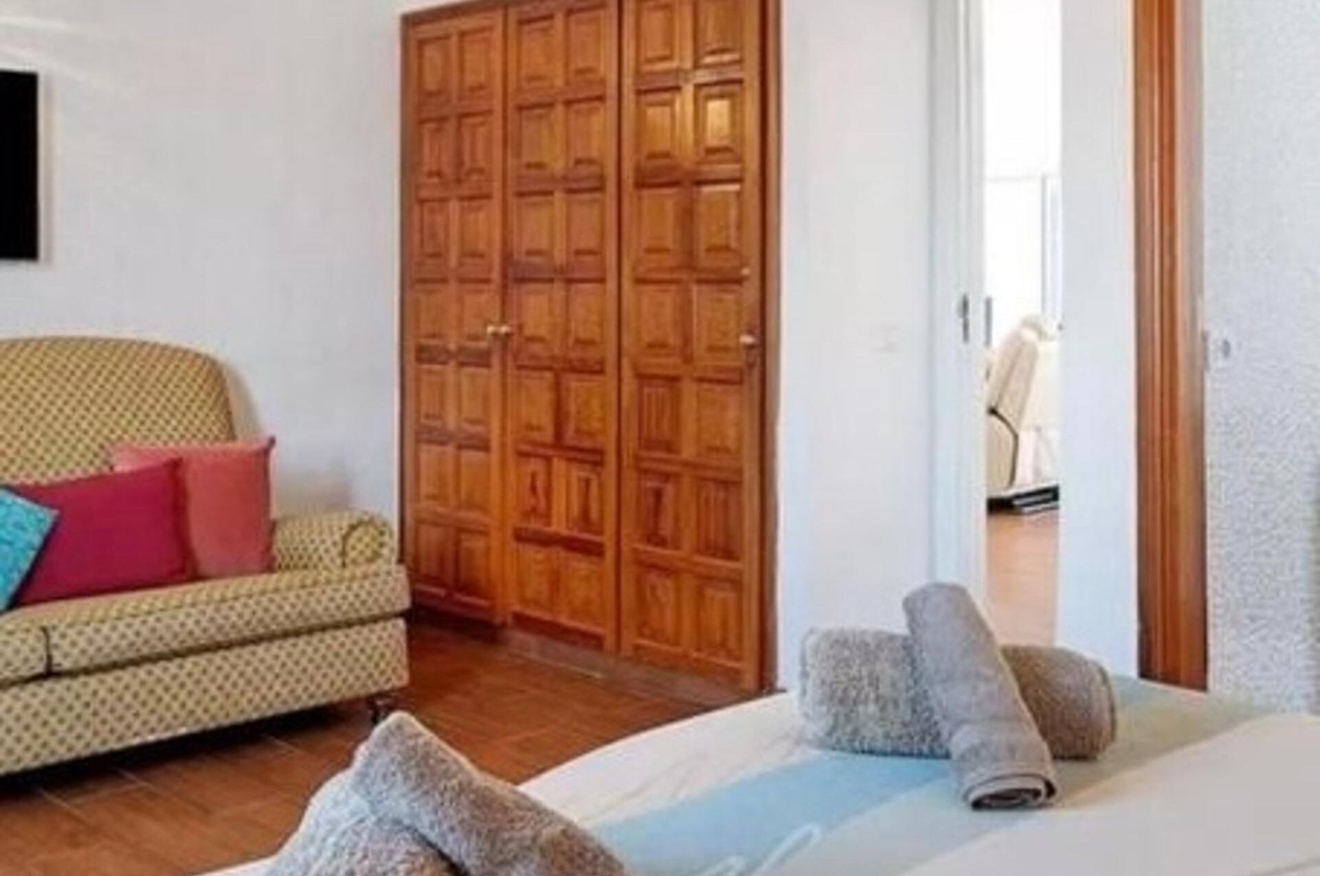 Una habitación con un sofá estampado, un armario de madera y una cama con toallas enrolladas.