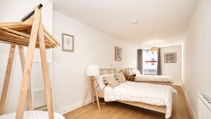 Ein Schlafzimmer mit einer Holzleiter, zwei Betten mit weißer Bettwäsche, einer Stehlampe und gerahmten Bildern an den Wänden.