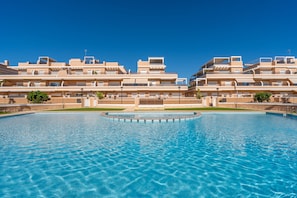 A swimming pool with a clear blue water surface, surrounded by a modern building with multiple balconies and a flat roof.