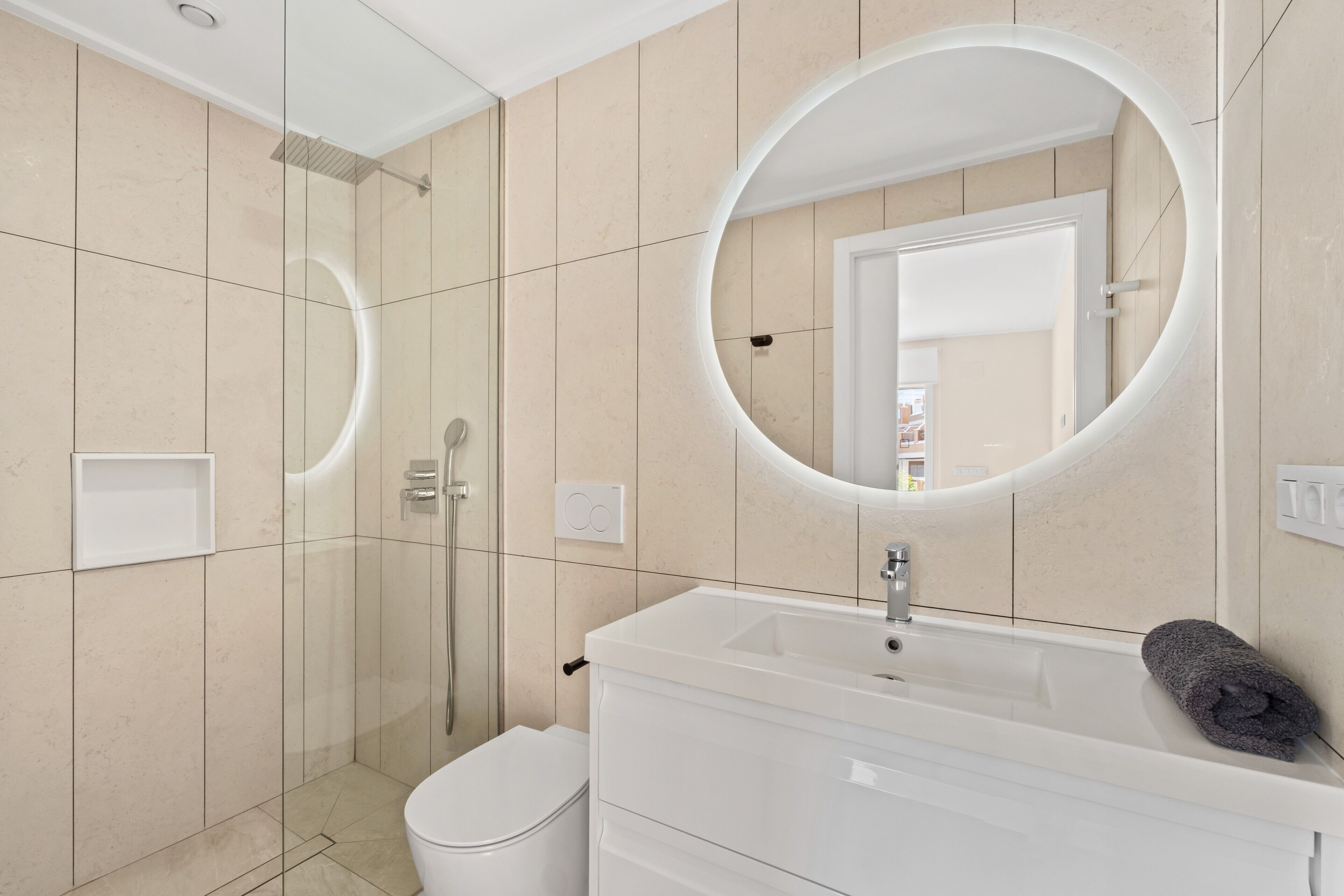Un baño moderno con ducha de vidrio, tocador blanco con lavamanos y un espejo grande.