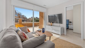 Una sala de estar moderna con un sofá, una mesa de centro, un televisor y un ventanal corredera que da a un balcón.