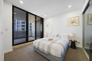 Ein modernes Schlafzimmer mit einem großen Bett, einer Glastür, die auf einen Balkon führt, und zwei gerahmten Kunstwerken an der Wand.