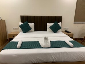 Una cama bien hecha con una colcha verde acolchada, dos almohadas y toallas enrolladas.