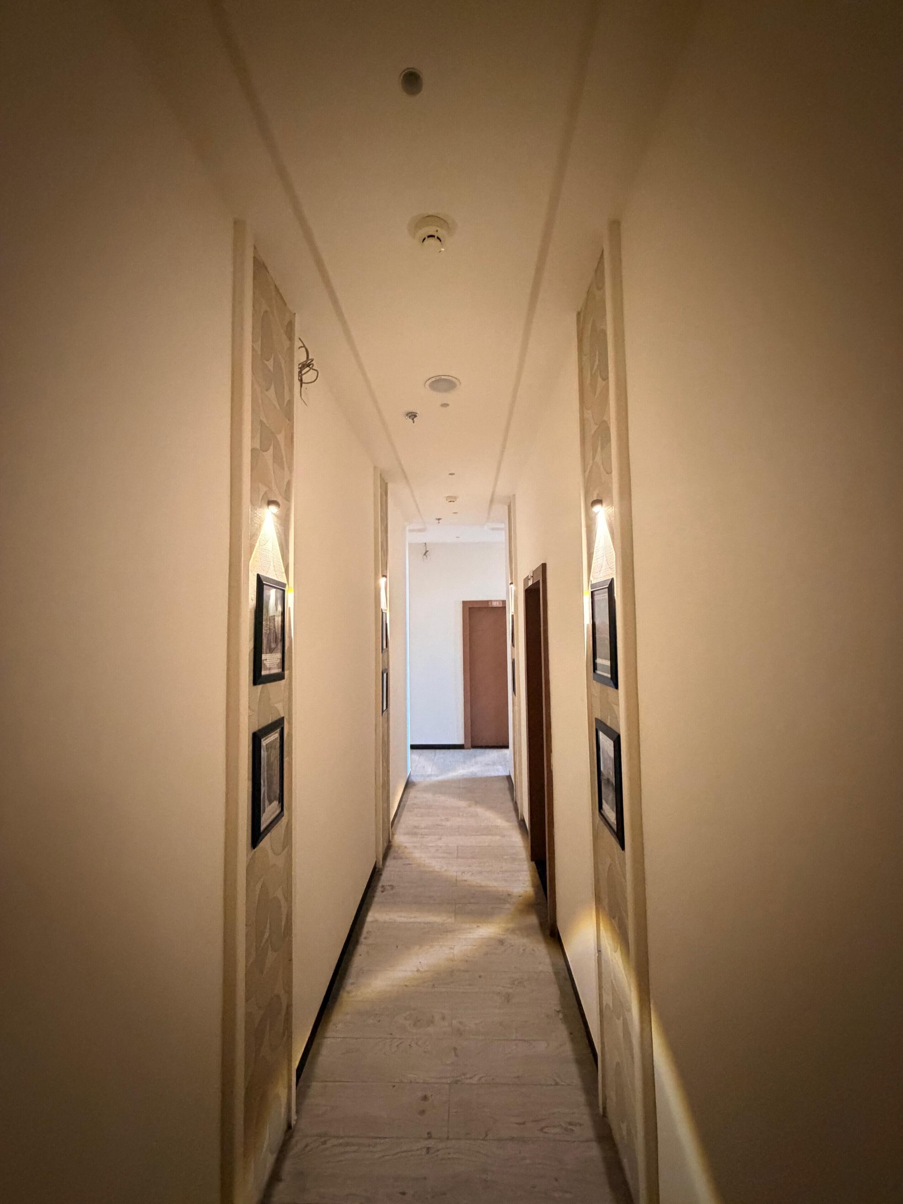 Un pasillo de hotel con cuadros enmarcados en las paredes, piso de madera y una puerta al final.
