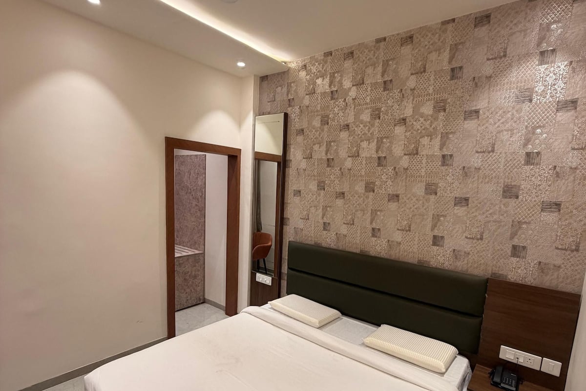 A modern bedroom with a bed, a nightstand, a mirror, a ceiling fan, and patterned wallpaper.