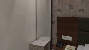 Habitación de hotel con cama, mesita de noche con teléfono y menú, interruptor de luz en la pared y un armario pequeño.
