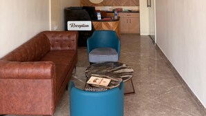 A modern reception area with a leather sofa, a blue chair, a marble coffee table, a chandelier, a clock, and a TV on the wall. - Hotel Tulsi Tower (Raipur)