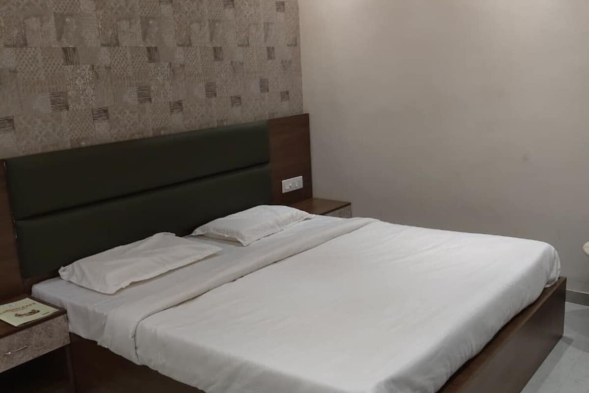 A single bed with white bedding, a green headboard, and a patterned wall behind it.