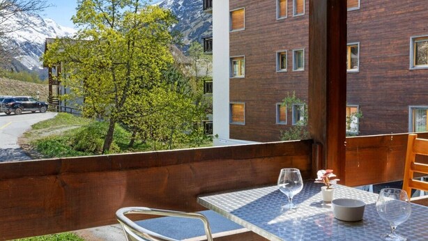 En balkon med et bord, stole og udsigt til et bjerg.