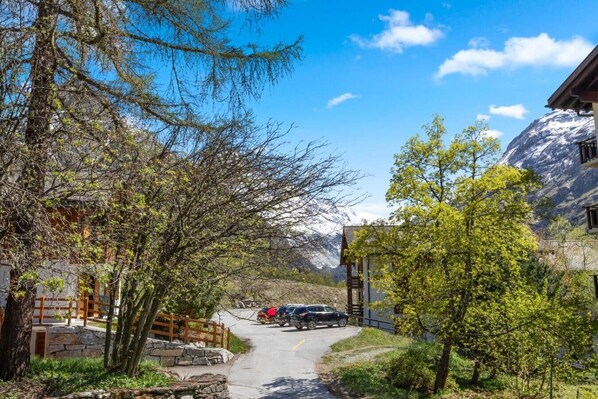 A mountain lodge with a stone pathway leading to a parking area, surrounded by trees and a mountain backdrop. - Convenient studio with view in the center of the resort (Anniviers)