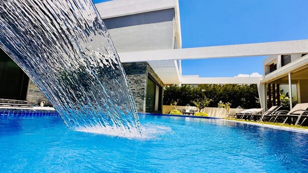 A swimming pool with a waterfall feature, lounge chairs, and a modern building in the background.