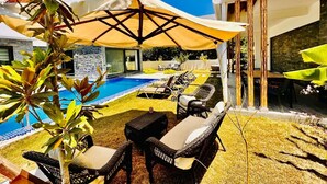 A poolside area with lounge chairs, a covered seating area, and a stone wall.