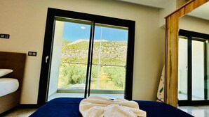 A hotel room with a bed, a large window with a view of a desert landscape, and a wooden door.