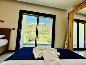 Una habitación de hotel con una cama, un ventanal con vistas a un paisaje desértico y una puerta de madera.