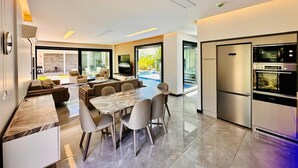 A modern kitchen with a built-in oven and microwave, a dining area with a marble table and chairs, and a large window overlooking a pool.