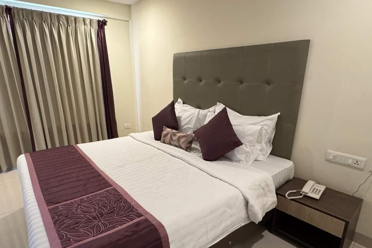 A neatly made bed with a headboard, a bedside table with a phone, and curtains on a window.