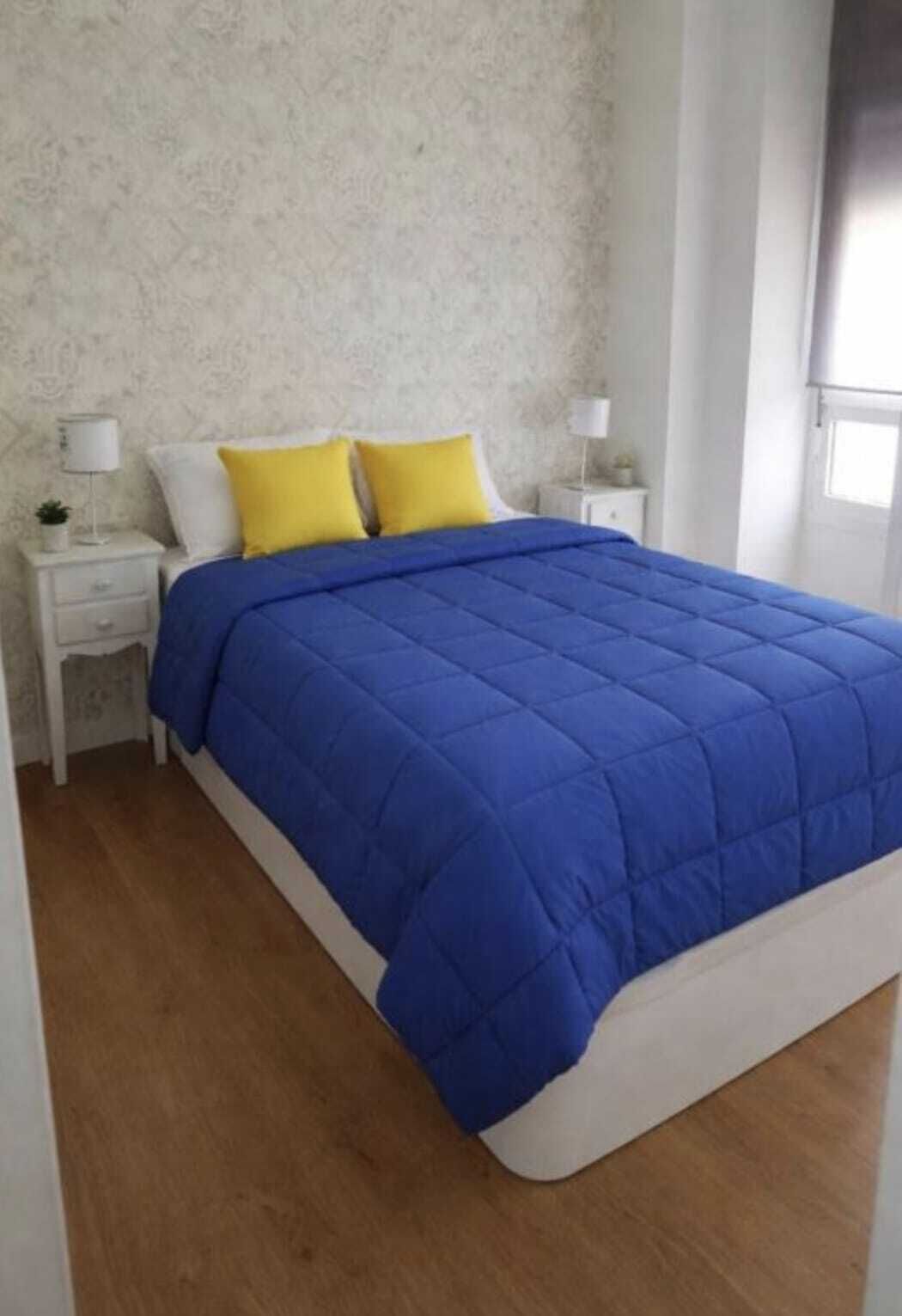 Una camera da letto con un letto, comodini bianchi, una coperta blu e cuscini gialli.