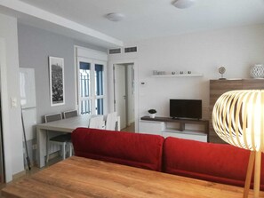 Eine moderne Küche mit Essbereich, einem Fernseher und einem roten Sofa.