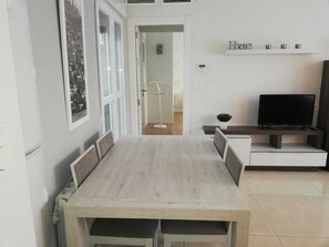 Un'area pranzo con un tavolo e sedie in legno, una televisione su un mobile e una porta che dà su un'altra stanza.