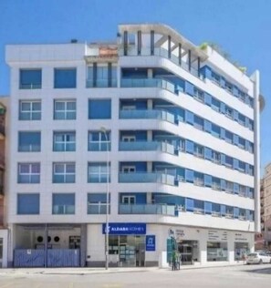 Un edificio a più piani con un design architettonico moderno, caratterizzato da balconi su ogni piano e un ingresso a livello strada.
