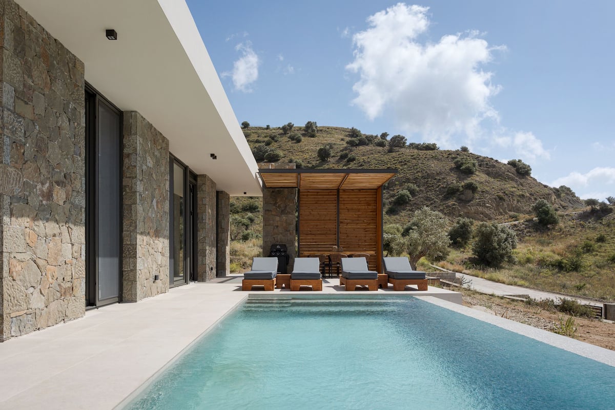 A modern pool area with stone walls, wooden deck, and lounge chairs.