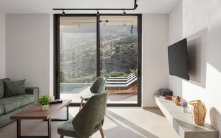 Un salon moderne doté d’une grande porte-fenêtre coulissante, d’un téléviseur à écran plat fixé au mur, d’un canapé, d’un fauteuil et d’une petite table sur laquelle est posée une plante.