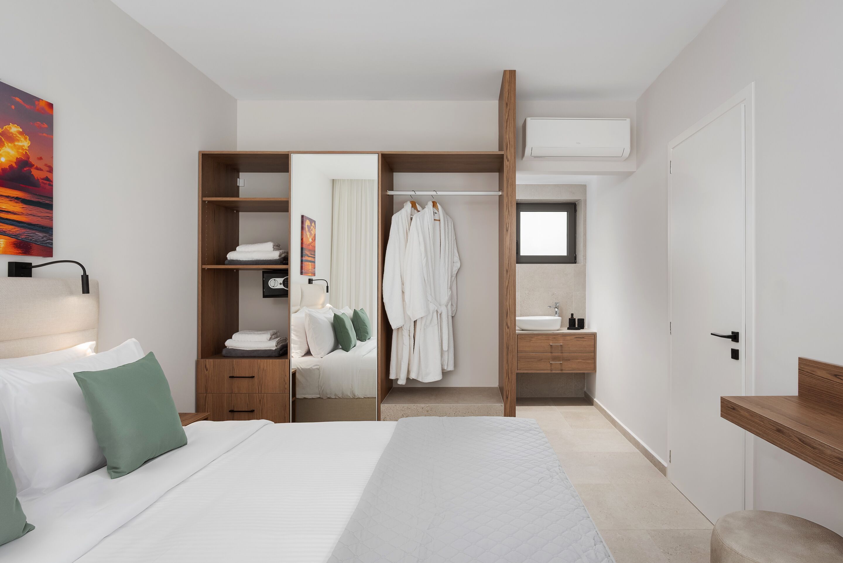 Une chambre d’hôtel moderne équipée d’un lit, d’un dressing, d’une salle de bain et d’une grande fenêtre.