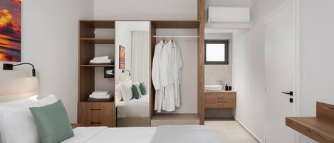 Une chambre d’hôtel moderne équipée d’un lit, d’un dressing, d’une salle de bain et d’une grande fenêtre.