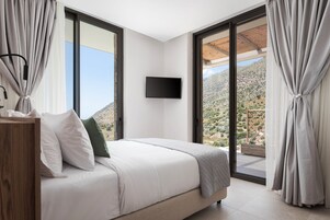 Une chambre dotée d’un lit, d’un téléviseur à écran plat et offrant une vue sur un paysage montagneux grâce  à de grandes fenêtres.