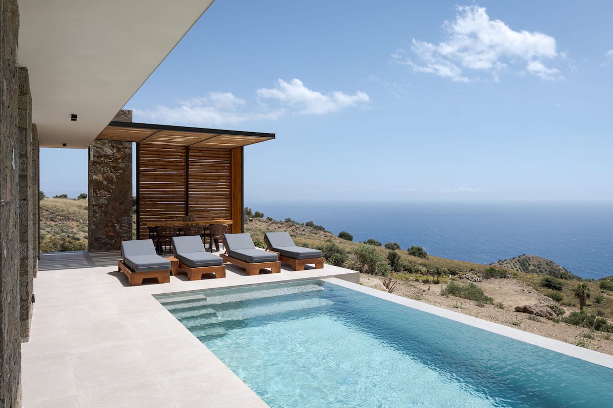 A modern outdoor pool area with lounge chairs and a view of the sea.