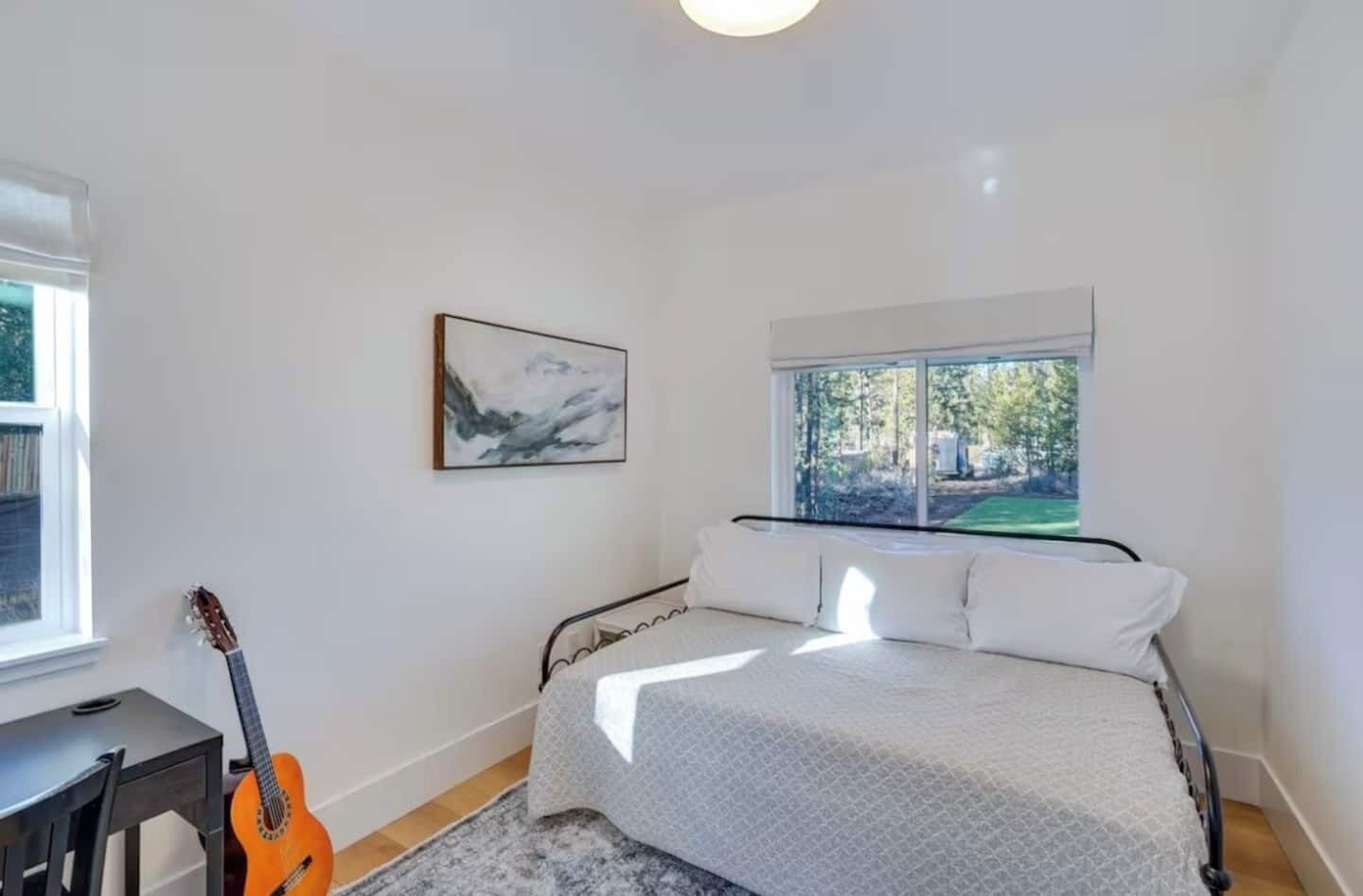 Quarto com cama, uma guitarra, uma janela e um quadro.
