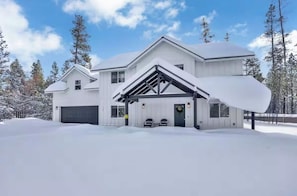 Ein modernes, zweistöckiges Haus mit Garage, bedeckt von Schnee, umgeben von Bäumen.