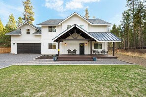 Ein zweistöckiges Haus mit überdachter Veranda, Garage und gepflegtem Rasen.