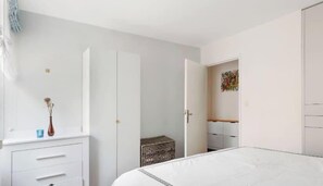 Ein Schlafzimmer mit Bett, Kleiderschrank, Kommode und einem kleinen Tisch mit Vase.