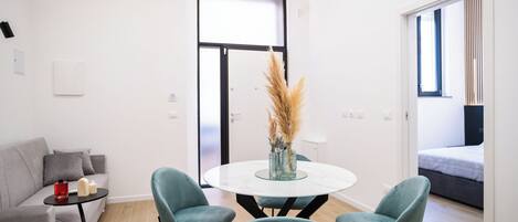 A modern living room with a round table, two teal chairs, a grey sofa, and a large window.