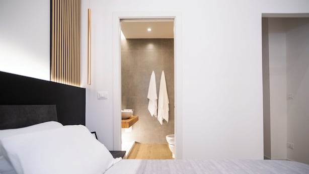 A modern hotel room with a bed, a bathroom with a toilet and sink, and a wooden shelf. - Cozy house 2 minutes from Reggio Calabria Cathedral and Via Marina (Reggio Calabria)