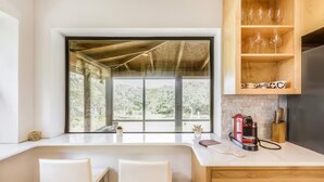 A modern kitchen with a large window, white bar stools, and a coffee machine. - Olinca Ranch - Private Texas Oasis (Driftwood)