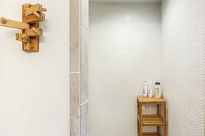 A bathroom with a wooden towel rack, a small wooden shelf with toiletries, and a textured wall. - Olinca Ranch (Driftwood)