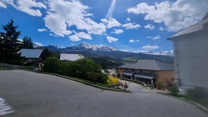 Une rue résidentielle bordée de maisons, avec un ciel dégagé et des montagnes enneigées en arrière-plan.