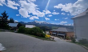 Eine Wohnstraße mit Häusern, blauem Himmel und schneebedeckten Bergen im Hintergrund.
