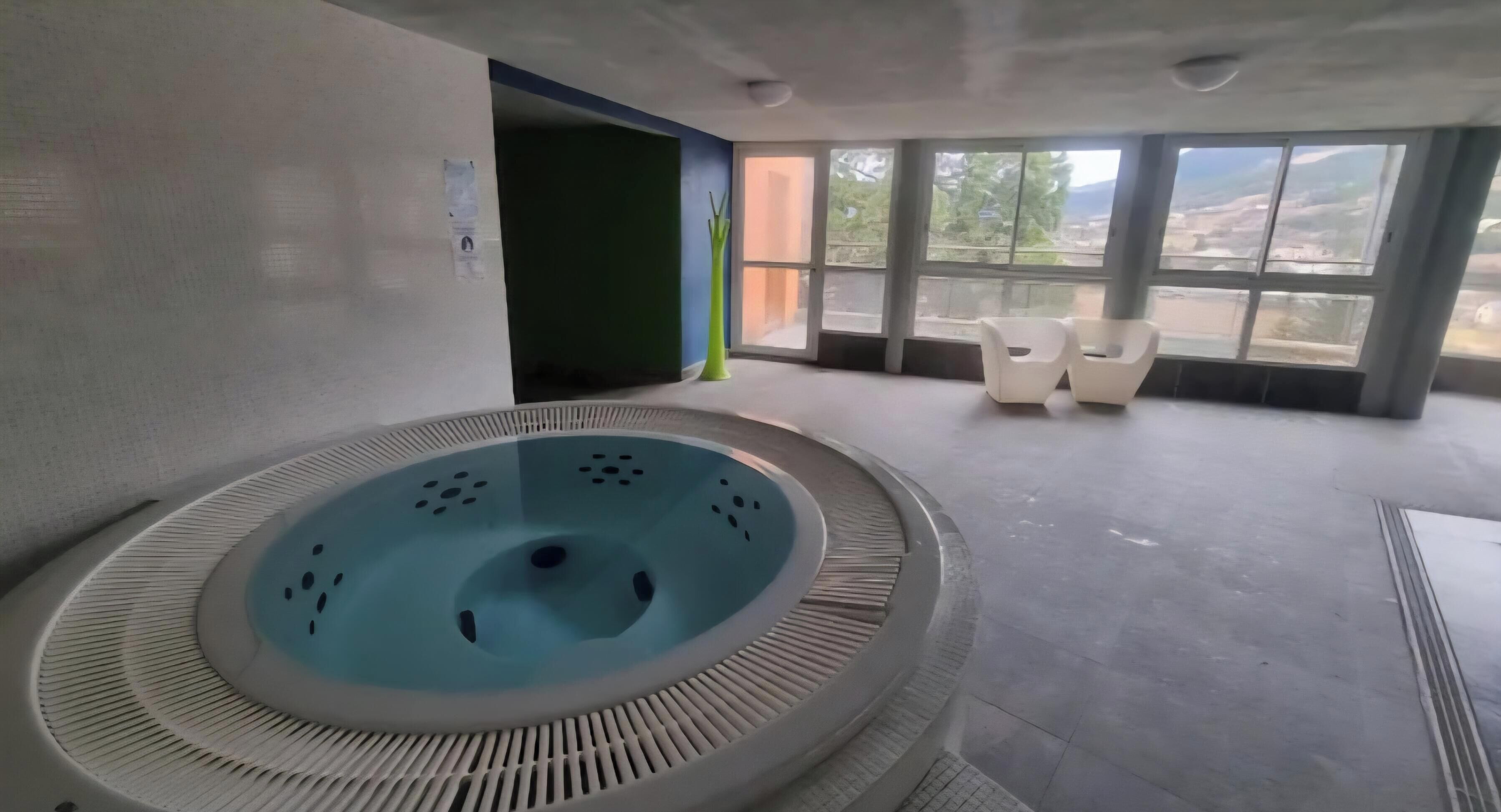 A spa area with a circular hot tub, a seating area with chairs, and large windows offering a view.